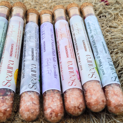 A collection of ‘Seaura Bath and Foot Salts’ products in various colors, indicating different scents or varieties. The products are arranged on a straw-like surface